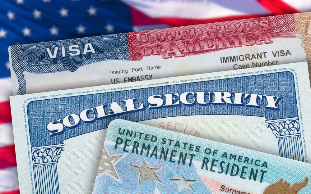 U.S. immigration documents stacked, including Social Security card, visa, and green card, with an American flag
