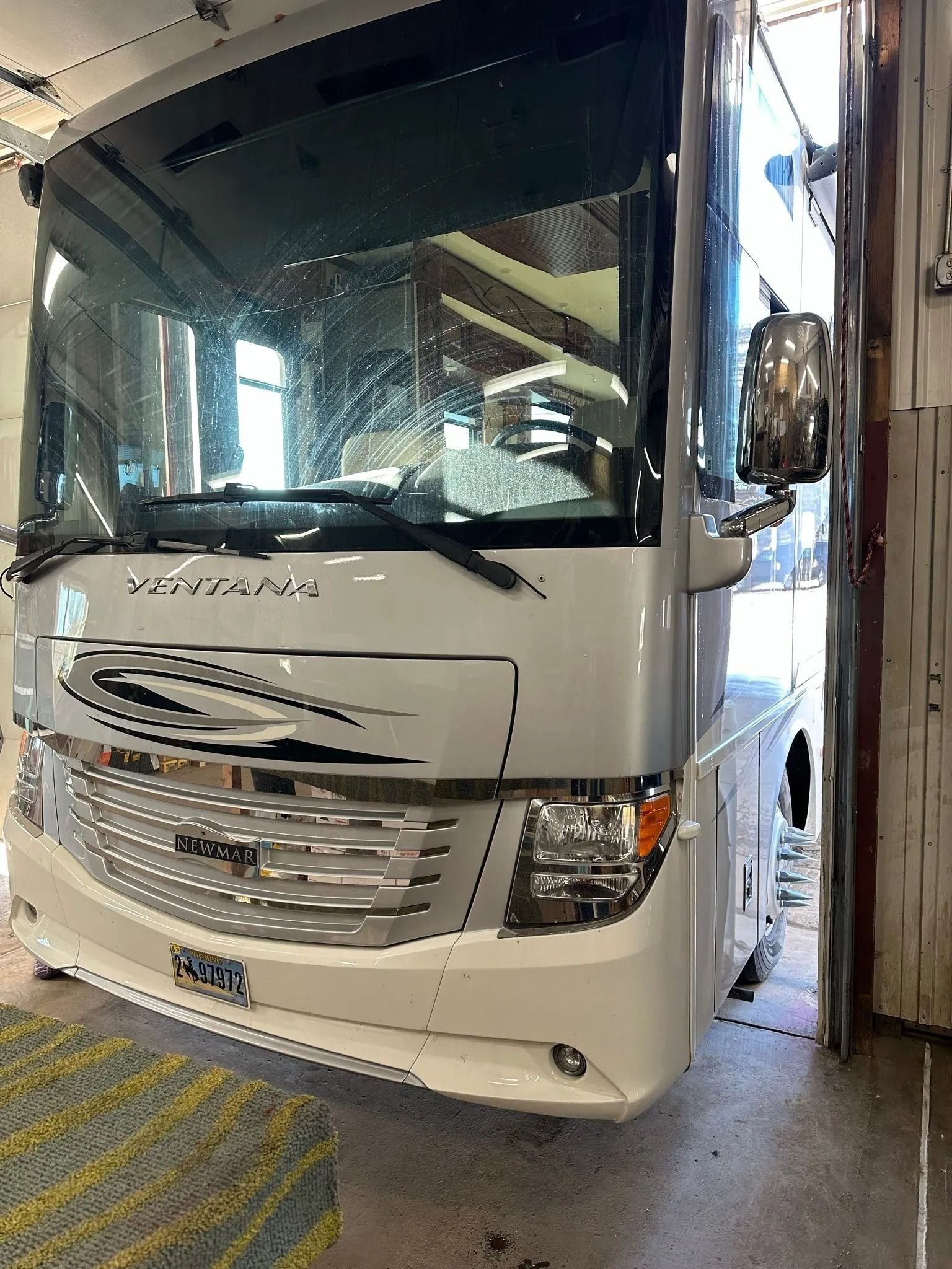 A front-facing view of a silver and white Class A motorhome parked inside a garage.