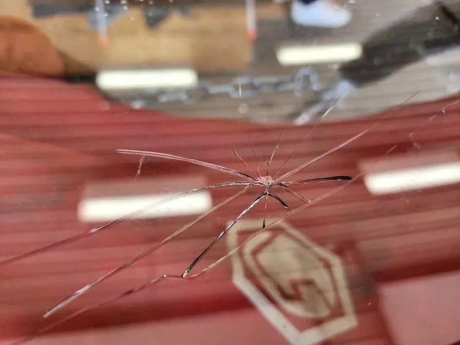 A close-up view of a small, star-shaped crack in a vehicle's windshield with multiple radiating lines.