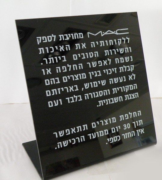שלט תצוגה שחור מפרספקס עם מדיניות ההחלפות של חברת MAC (מאק) מודפסת בלבן, המדגים איכות הדפסה גבוהה על חומרים קשיחים המבוצעת לרוב כחלק משירותי הדפסת קטלוג בחולון למותגים.