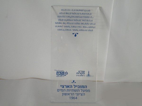 לוח פרספקס שקוף ואלגנטי המנציח את פרויקט המוביל הארצי של חברת מקורות עם הדפסת טקסט בכחול, הממחיש איכות הדפסה מדויקת על חומרים קשיחים באמצעות דפוס דיגיטלי בחולון.