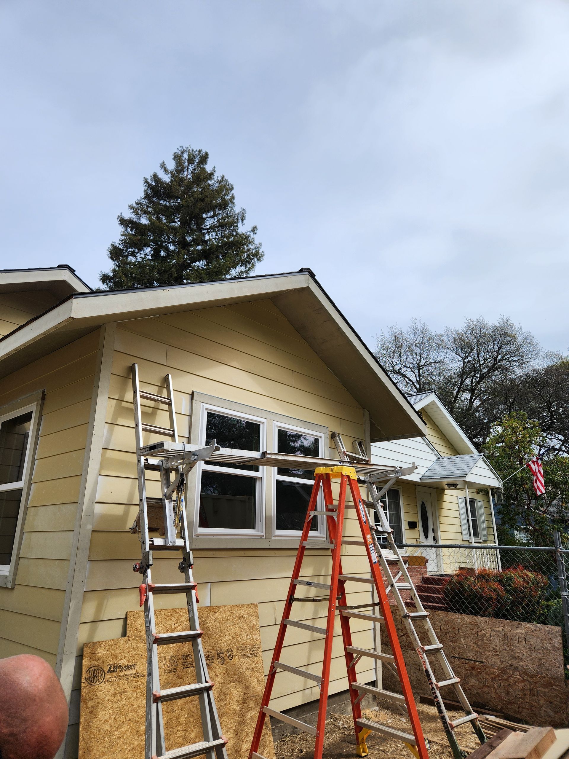 Lap siding replacement underway on a single-story home, with ladders at the front gable