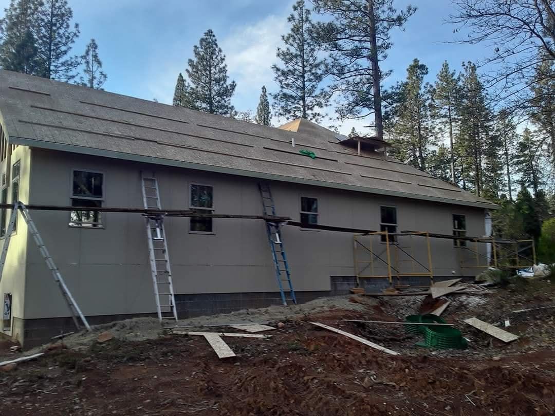 Gray lap siding going up on a long single-story wall, with ladders in place