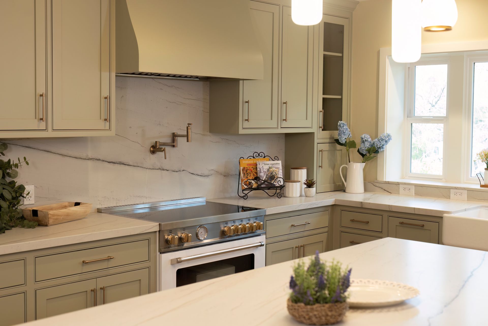 A modern kitchen with sage green cabinets, white countertops, and a large range.