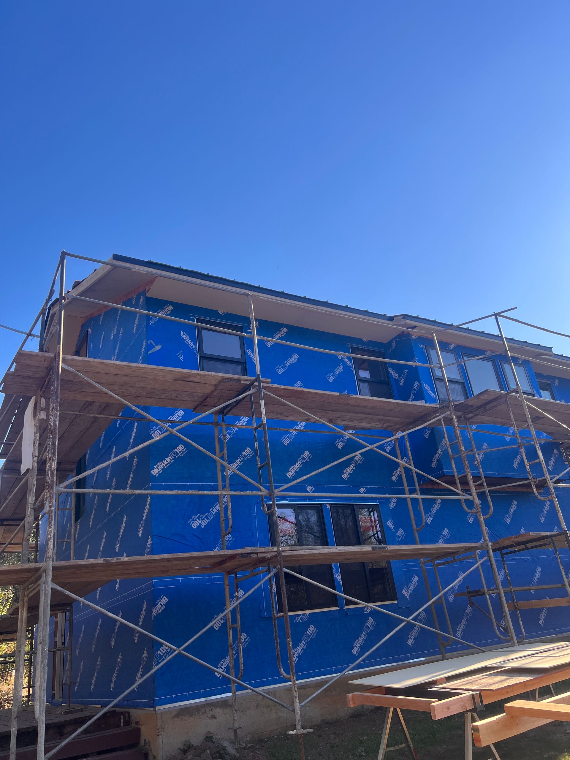 Blue peel-and-stick air barrier covering a two-story home behind scaffolding, before new siding
