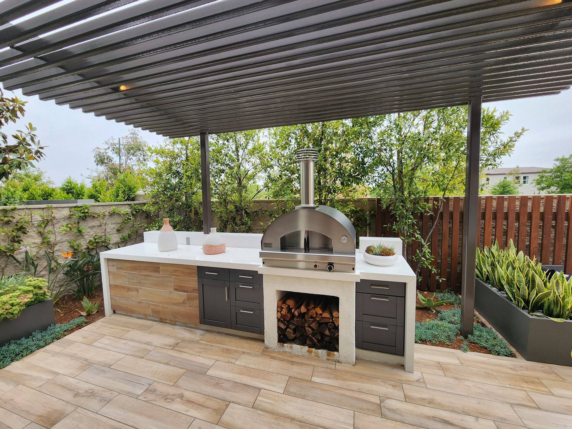 Outdoor kitchen with a pergola and built-in grill in a fenced backyard