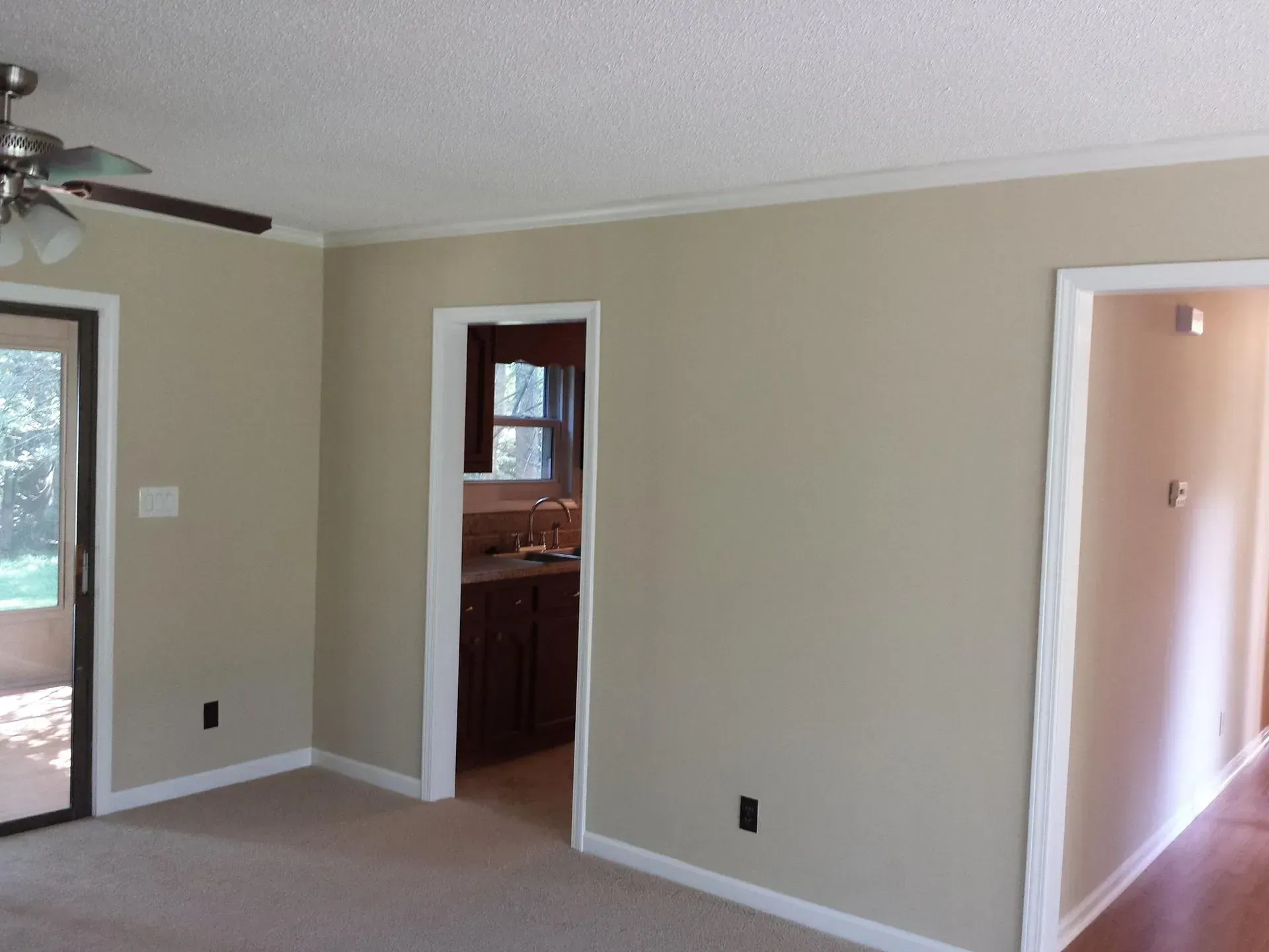Beige walls in a room with white trim, a door to outside, and two other doorways.