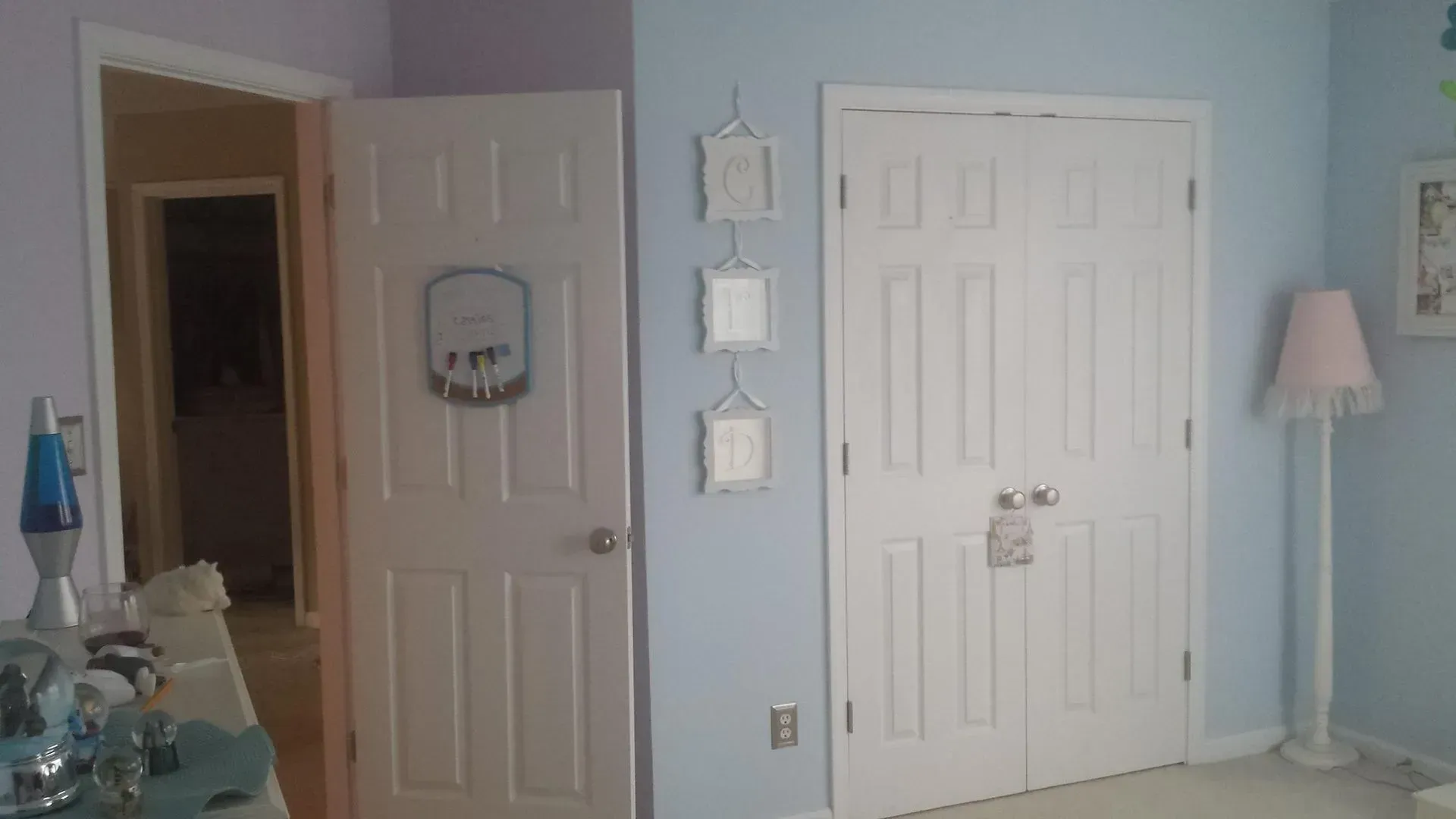 Bedroom interior: white doors, blue walls, decorative frames, a lamp with a pink shade, and a lava lamp.