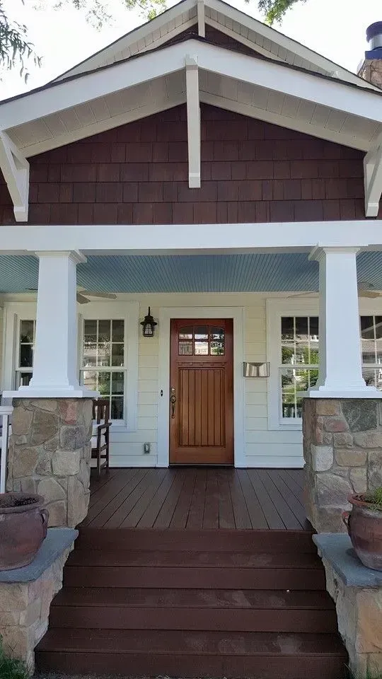 Craftsman-style home exterior with brown door, porch with white columns, and stone accents.