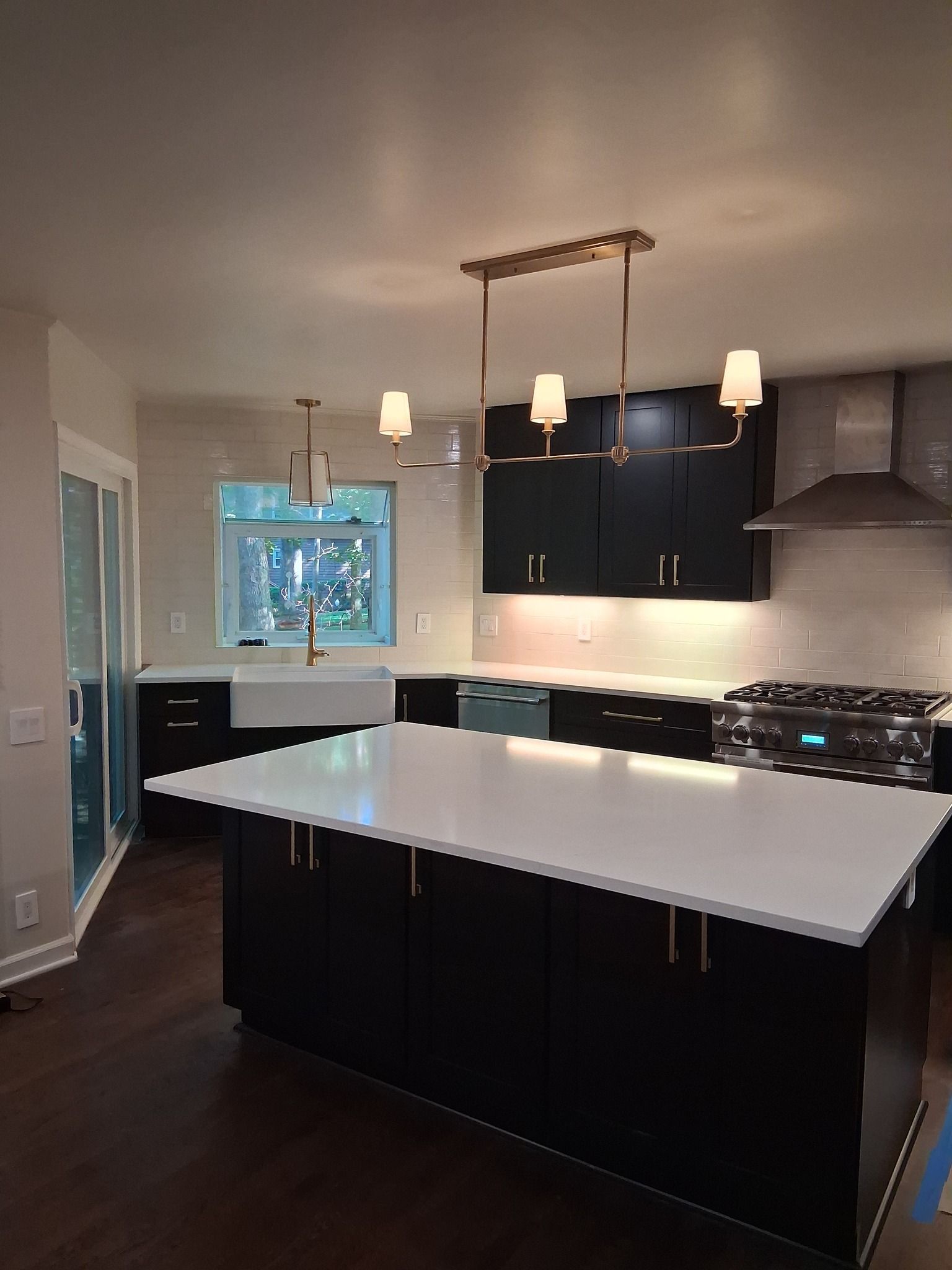 Modern kitchen with black cabinets, white countertops, island, and gold light fixtures.