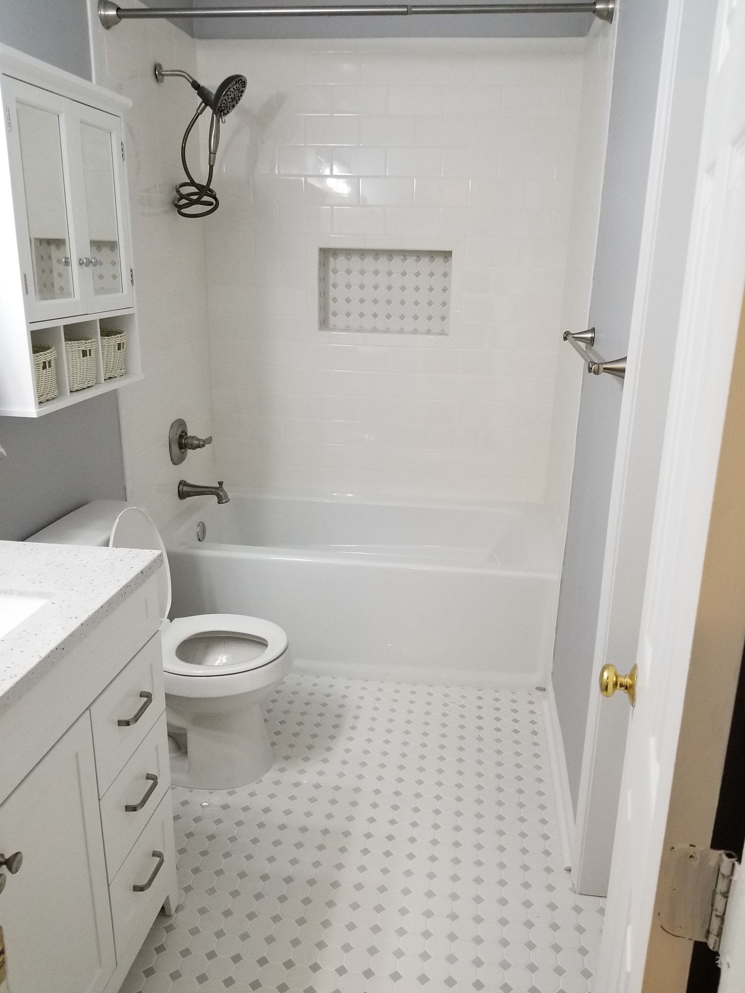 White bathroom with shower/tub combo, toilet, vanity, and small tile floor.