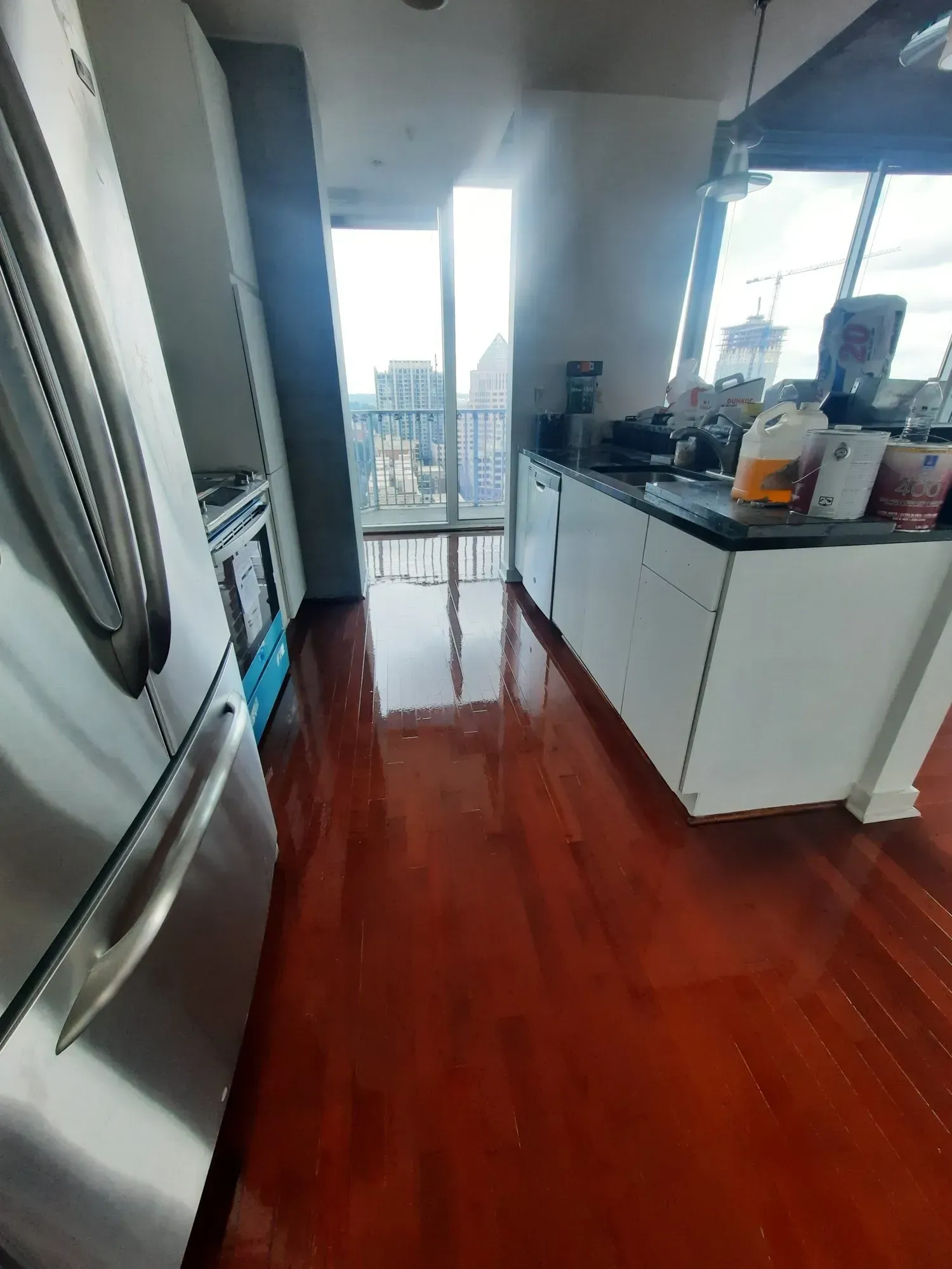 Red-floored kitchen with stainless steel refrigerator, white cabinets, and large window overlooking cityscape.