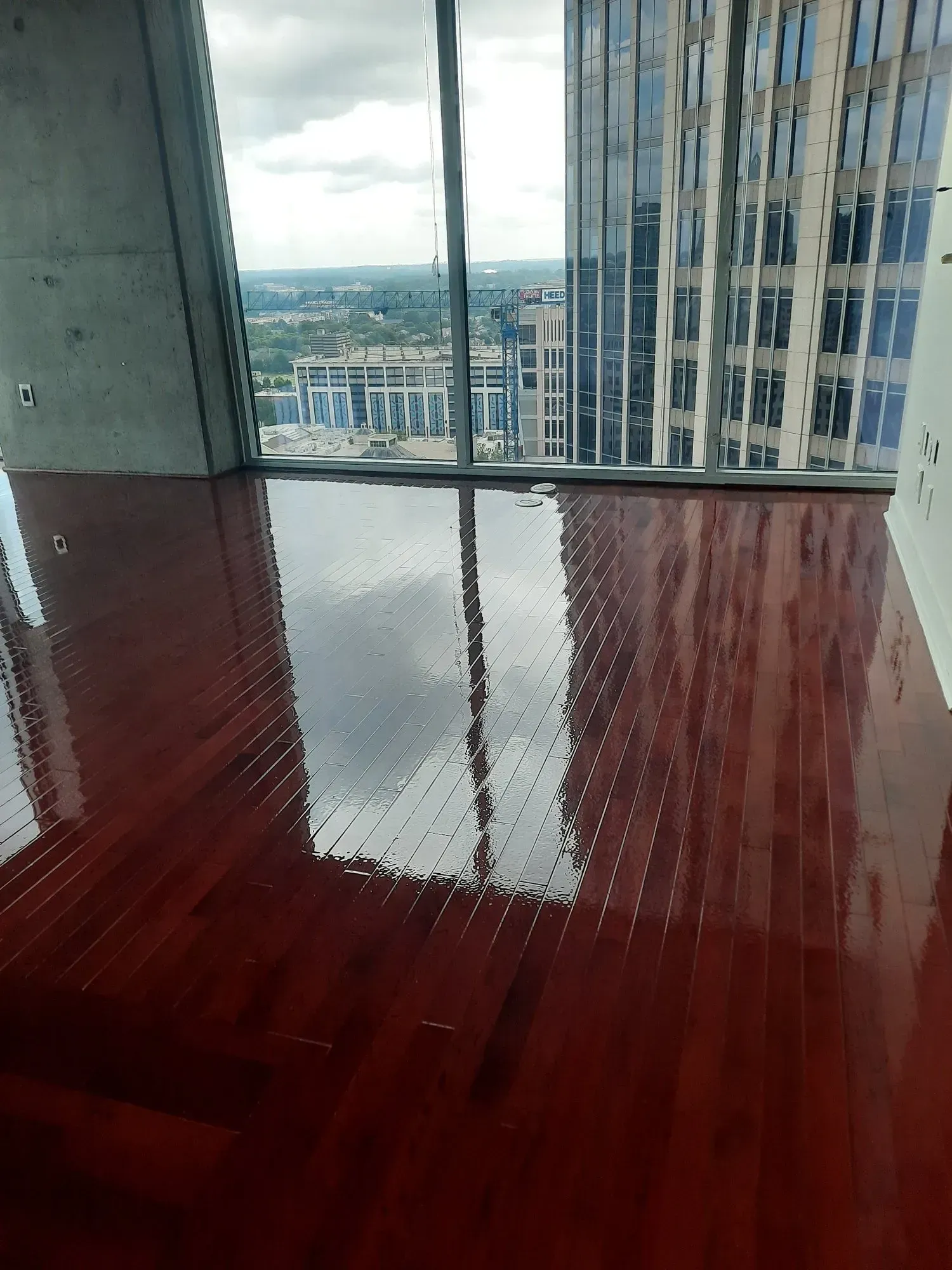 Red glossy wooden floor reflecting a city view through a large window. High-rise buildings visible outside.