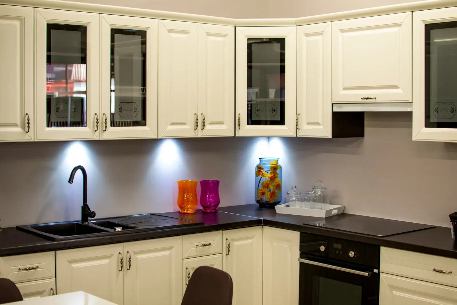 White kitchen cabinets with black countertops and sink; under-cabinet lighting.