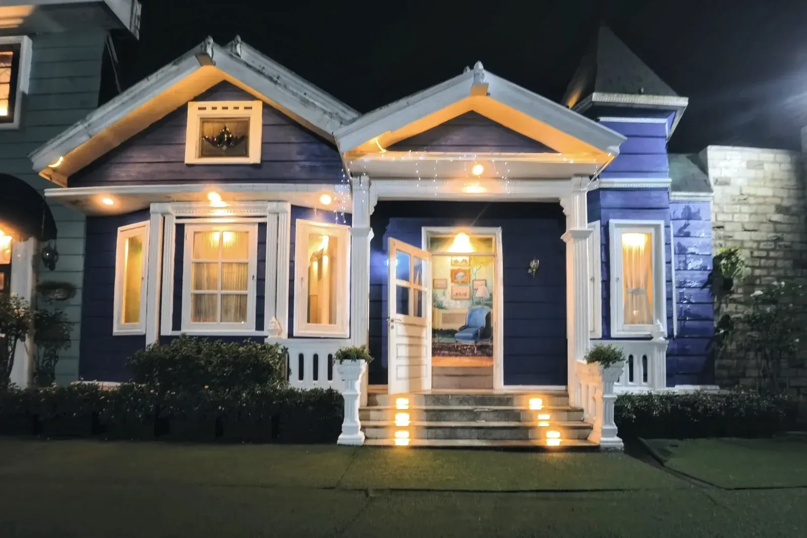 Blue house lit up at night, with white trim and glowing windows and open door.