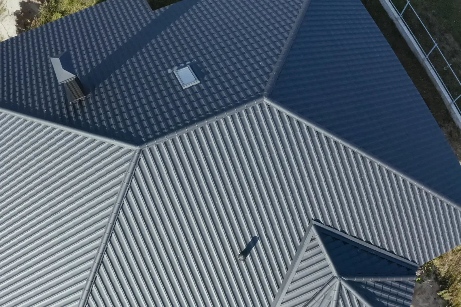 Dark gray corrugated metal roof of a house with different sections and a chimney.