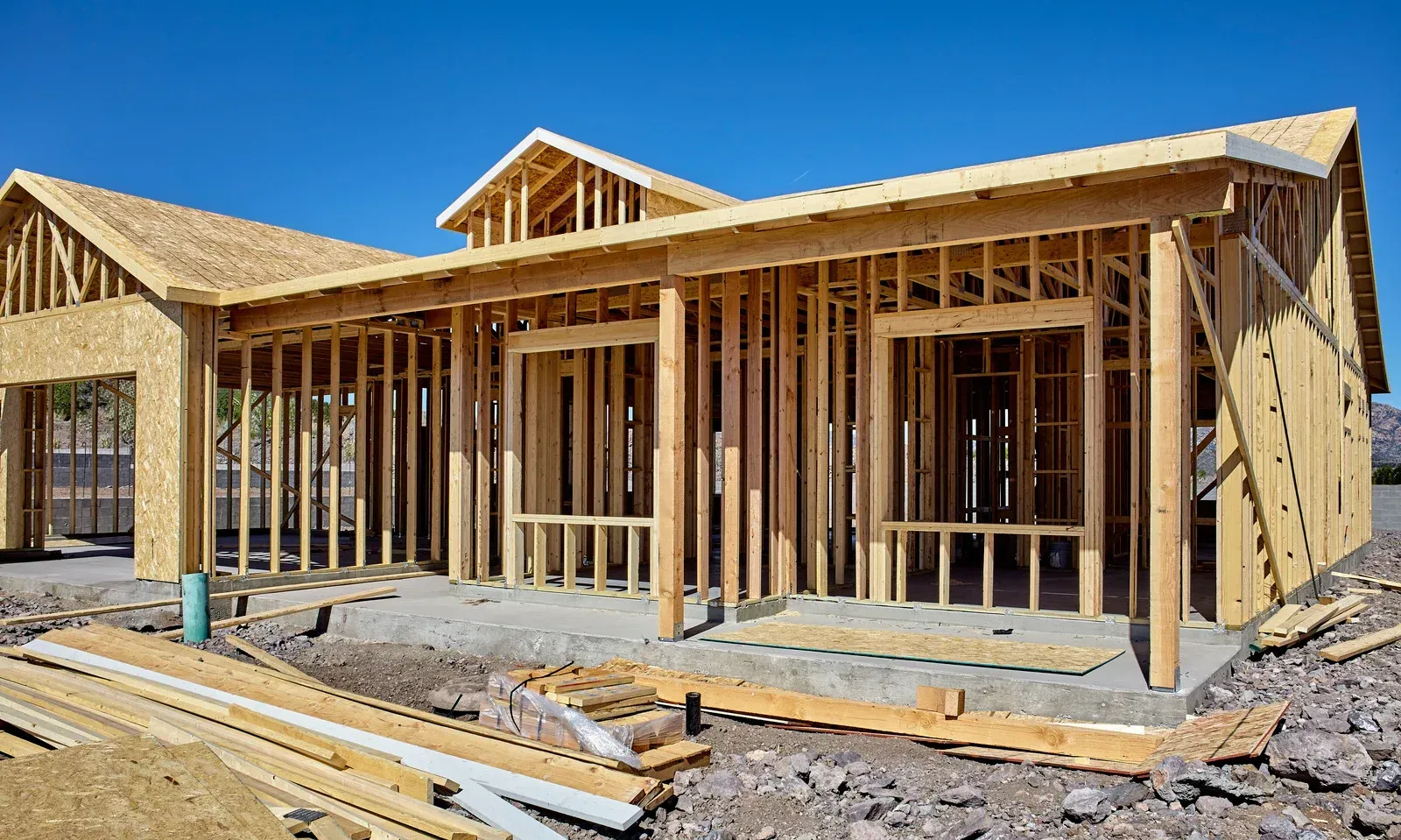 Wooden frame of a house under construction on a concrete foundation, with a blue sky.