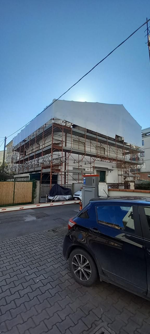 Edificio d'angolo in fase di ristrutturazione su una strada acciottolata, con un'auto nera parcheggiata davanti.