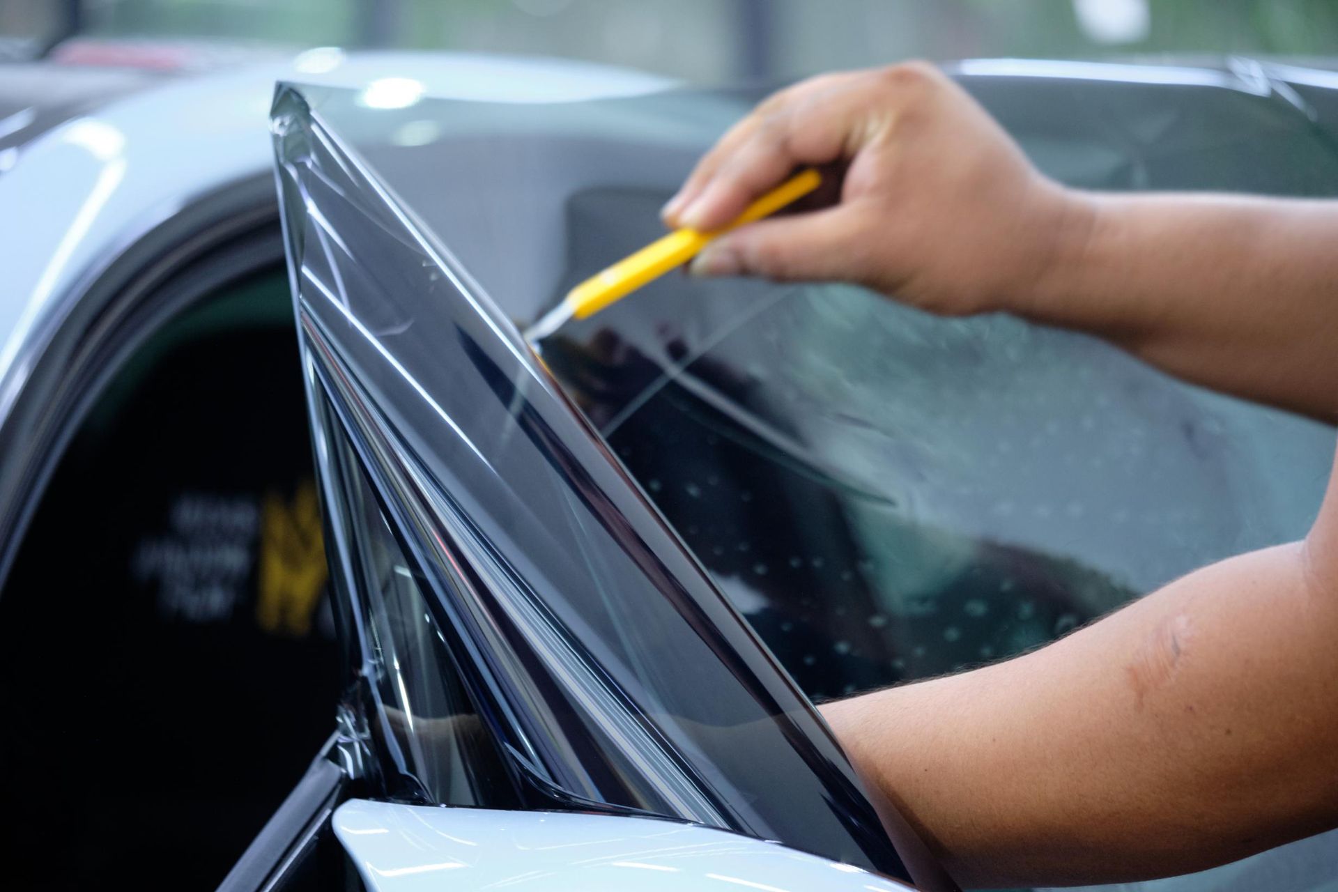 Hand washing a car window with a yellow sponge
