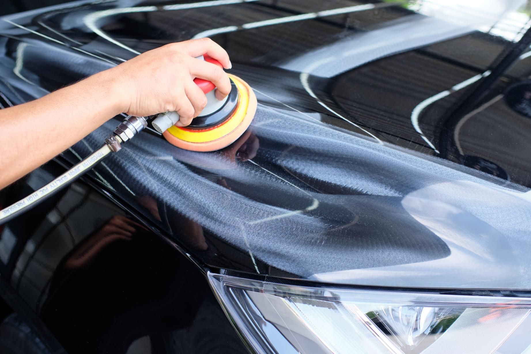 Hand polishing a black car hood with a buffer, creating a glossy finish