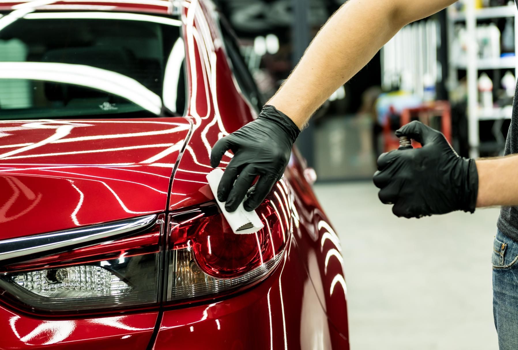 Person polishing a red car’s rear taillight in an auto shop