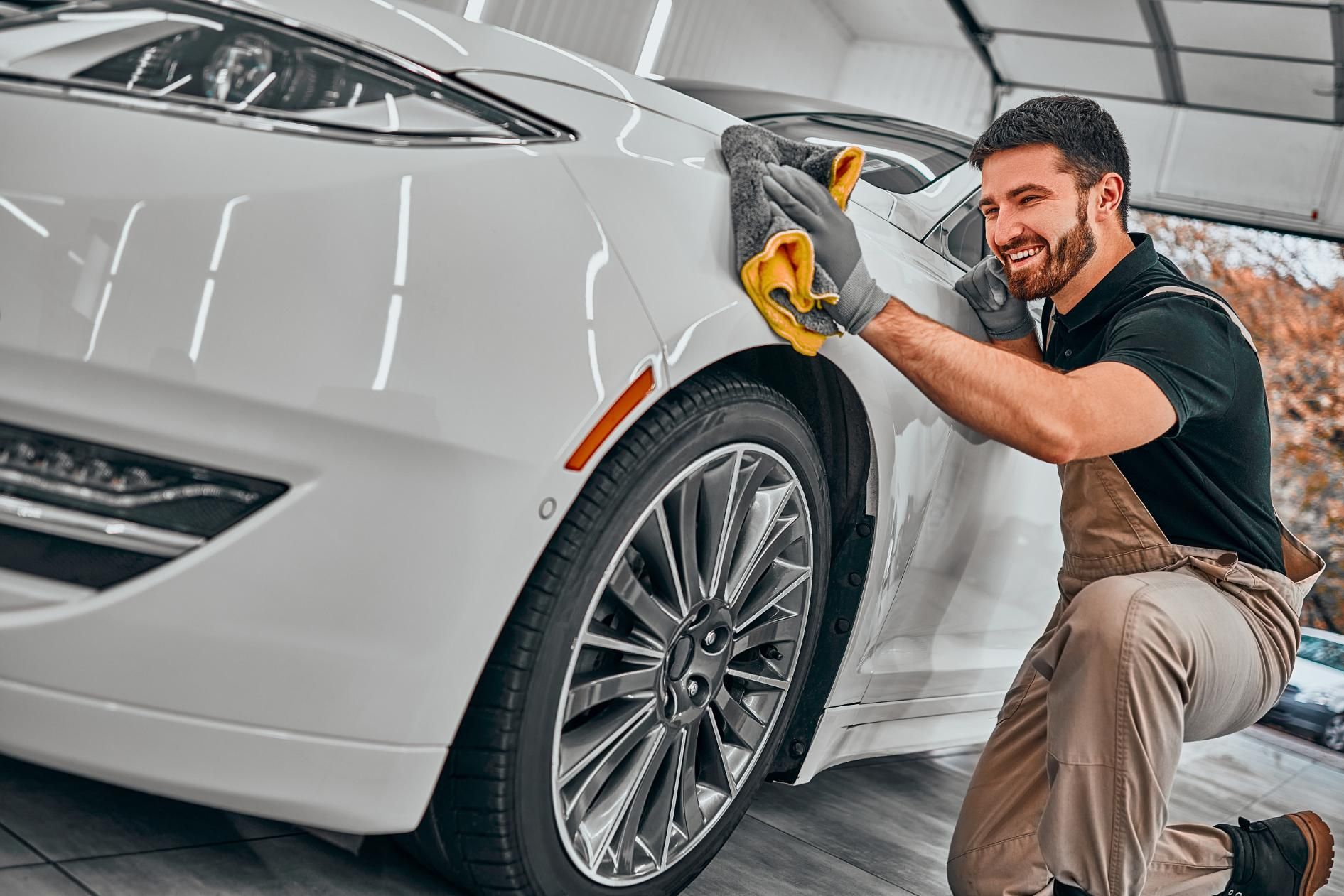 Man polishing a white car with a cloth in a bright auto detailing garage