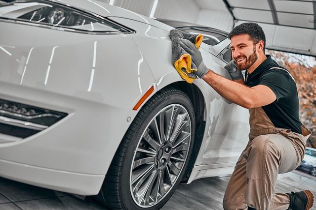 Detailer polishing a white car in a garage with a yellow cloth