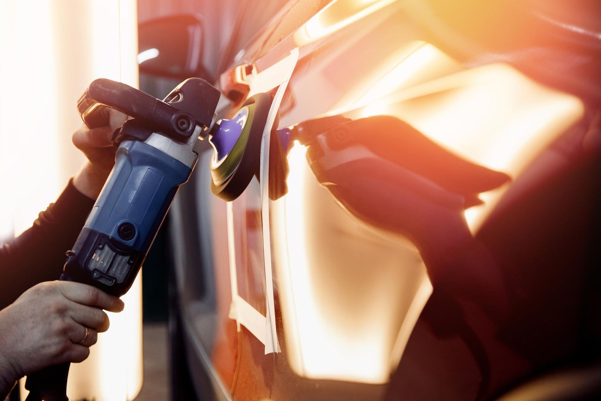 Hand holding a blue electric vehicle charging plug beside a car at sunset