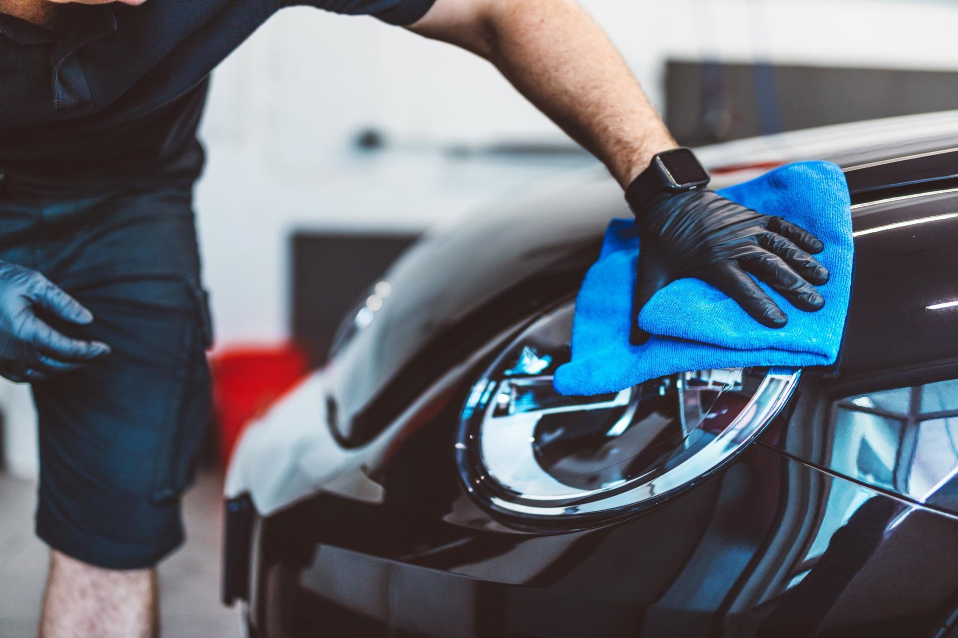 Person wiping a black car’s headlight with a blue cloth while wearing black gloves