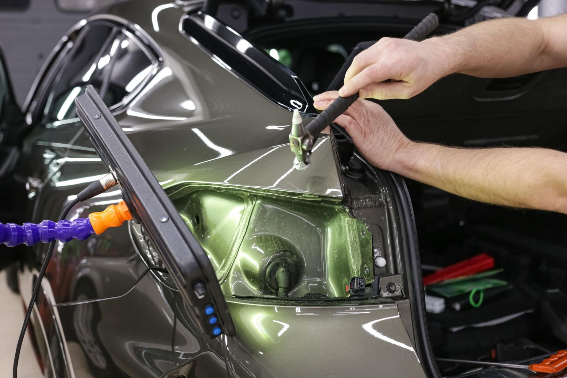 Technician spray-painting a dark green car door in an auto body shop