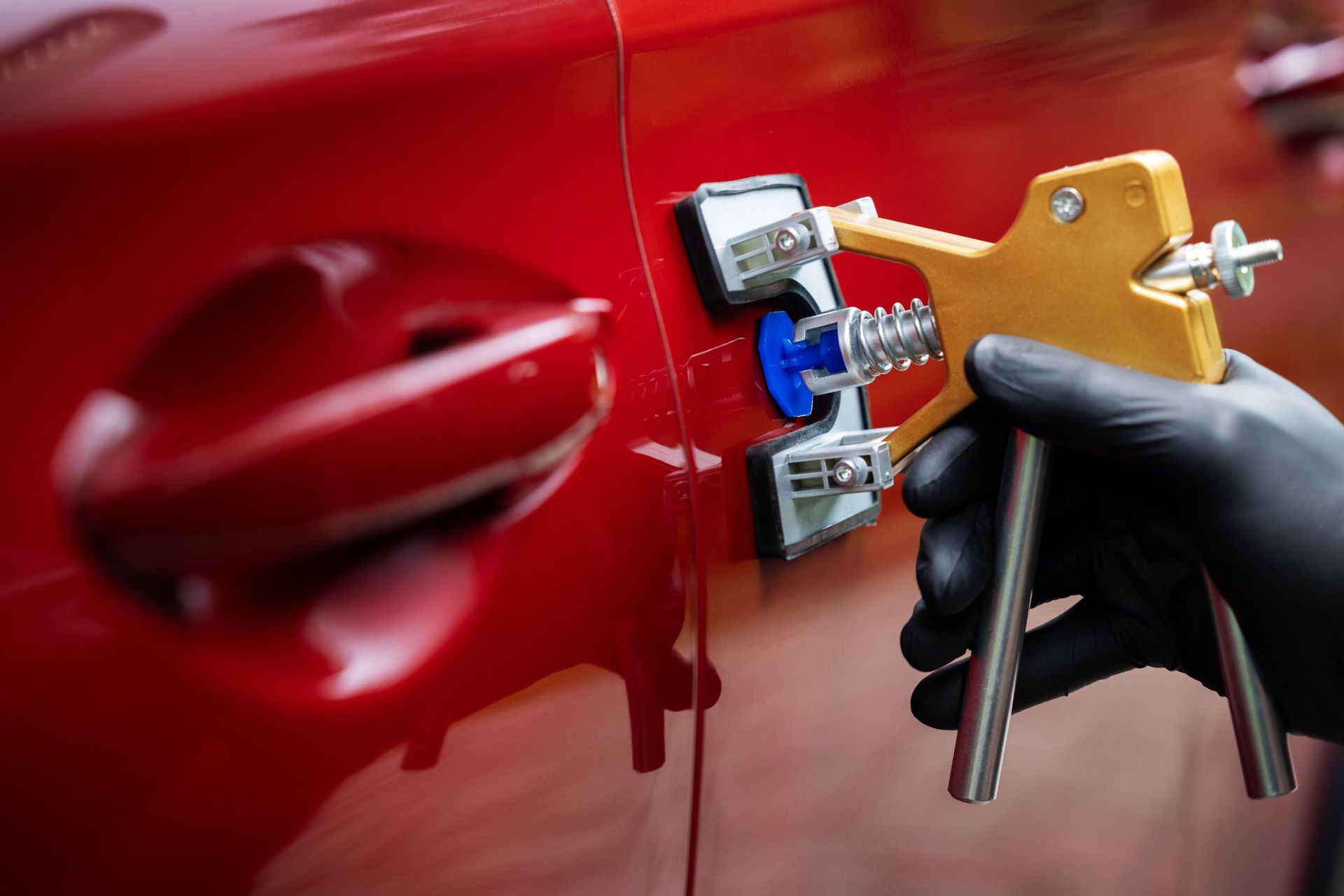 Gloved hand using a key on a red car door lock with a key fob nearby
