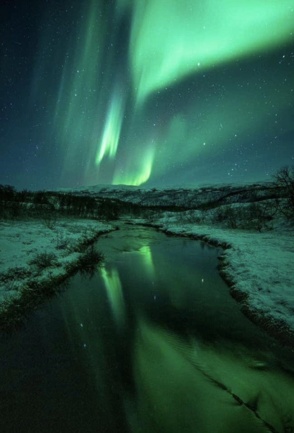 Das Polarlicht spiegelt sich im Wasser eines Flusses.