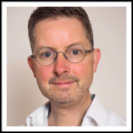 Ein Mann mit Brille und weißem Hemd lächelt in die Kamera.