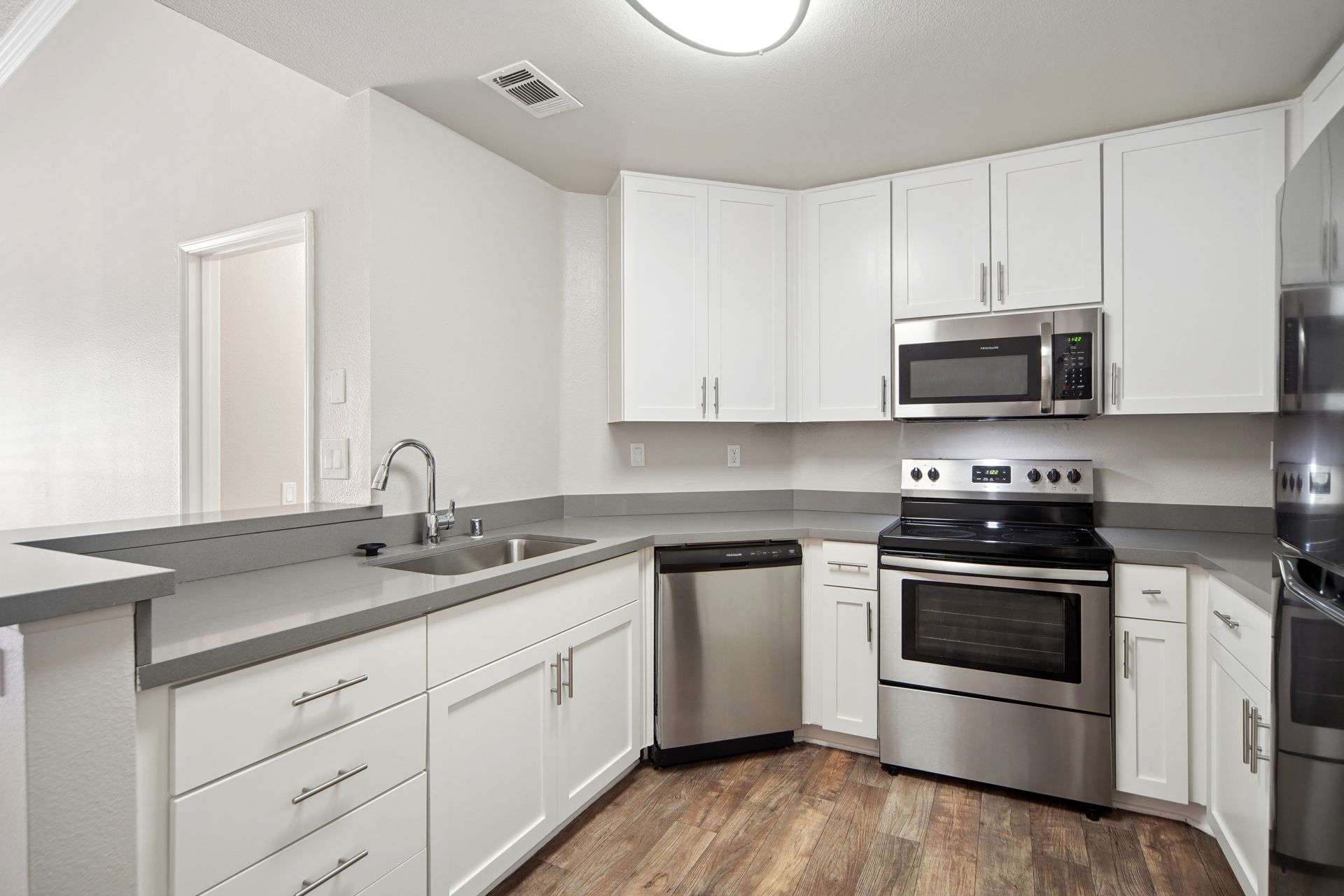 Bright white kitchen with stainless steel appliances, gray countertops, and wood flooring