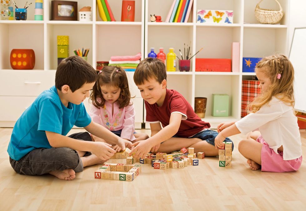 Bambini che giocano con i mattoncini su un pavimento di legno in una luminosa stanza dei giochi.