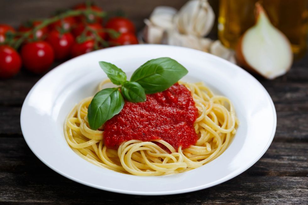 Piatto di spaghetti al sugo di pomodoro e basilico, con pomodori e aglio sullo sfondo.