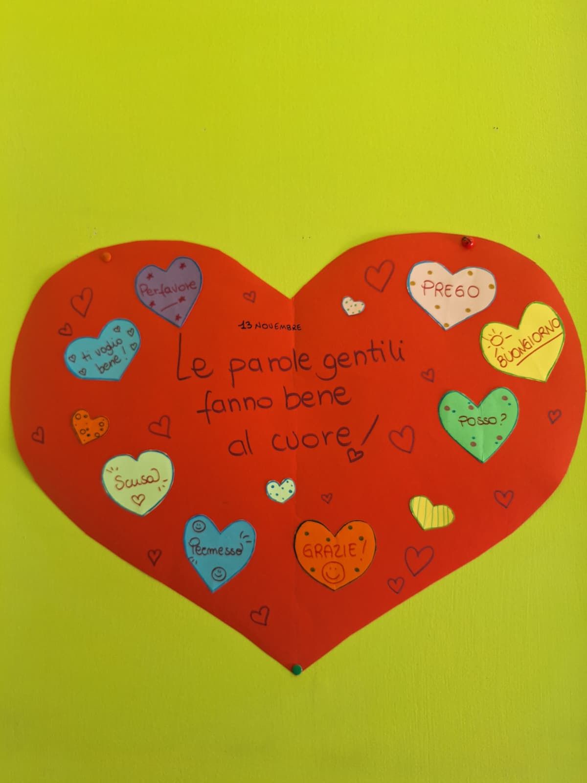 Biglietto a forma di cuore rosso su sfondo giallo con piccoli cuoricini colorati e messaggio scritto a mano in italiano.