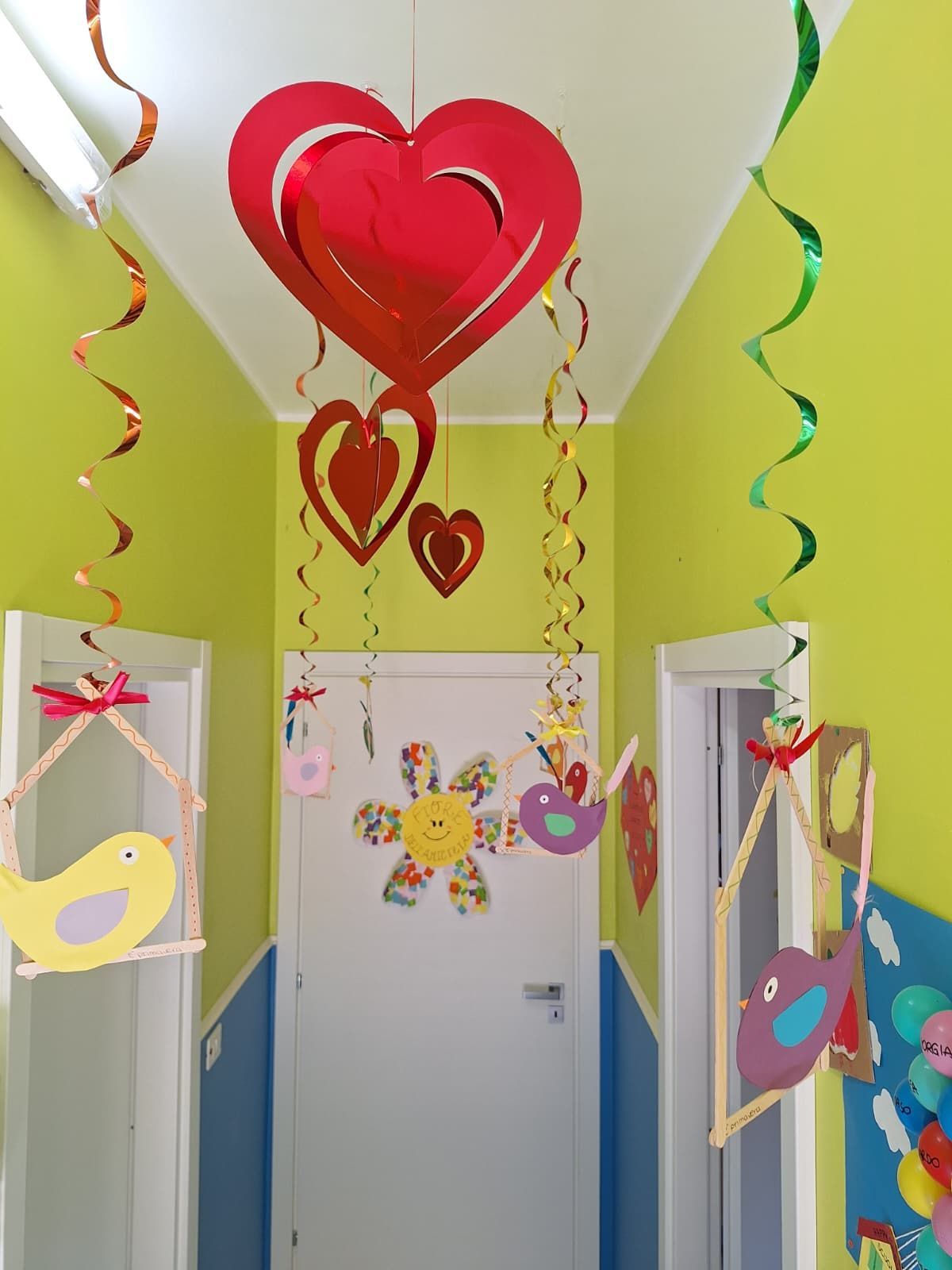 Decorazioni di San Valentino a forma di cuore appese in un corridoio con festoni colorati e ritagli di carta.
