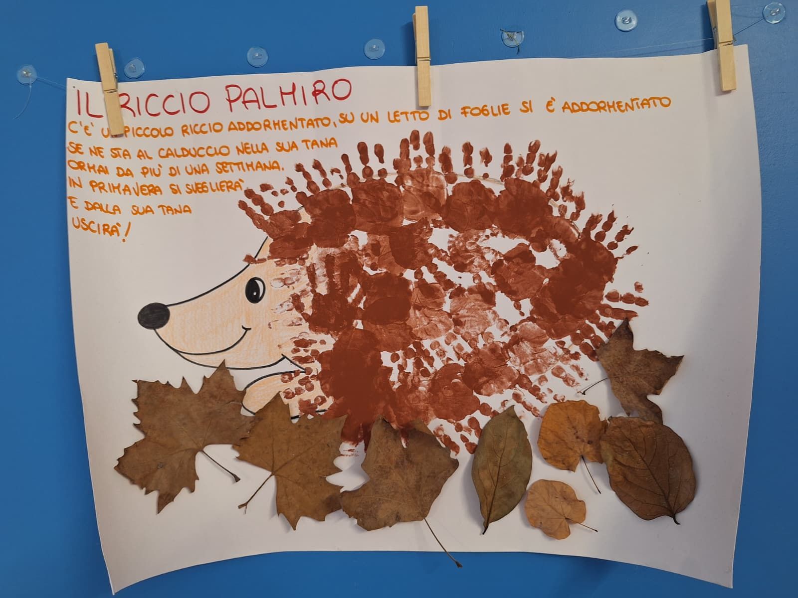 Lavoretto per bambini a forma di riccio con foglie marroni e un corpo a forma di impronta di mano rossa, fissato a un filo.