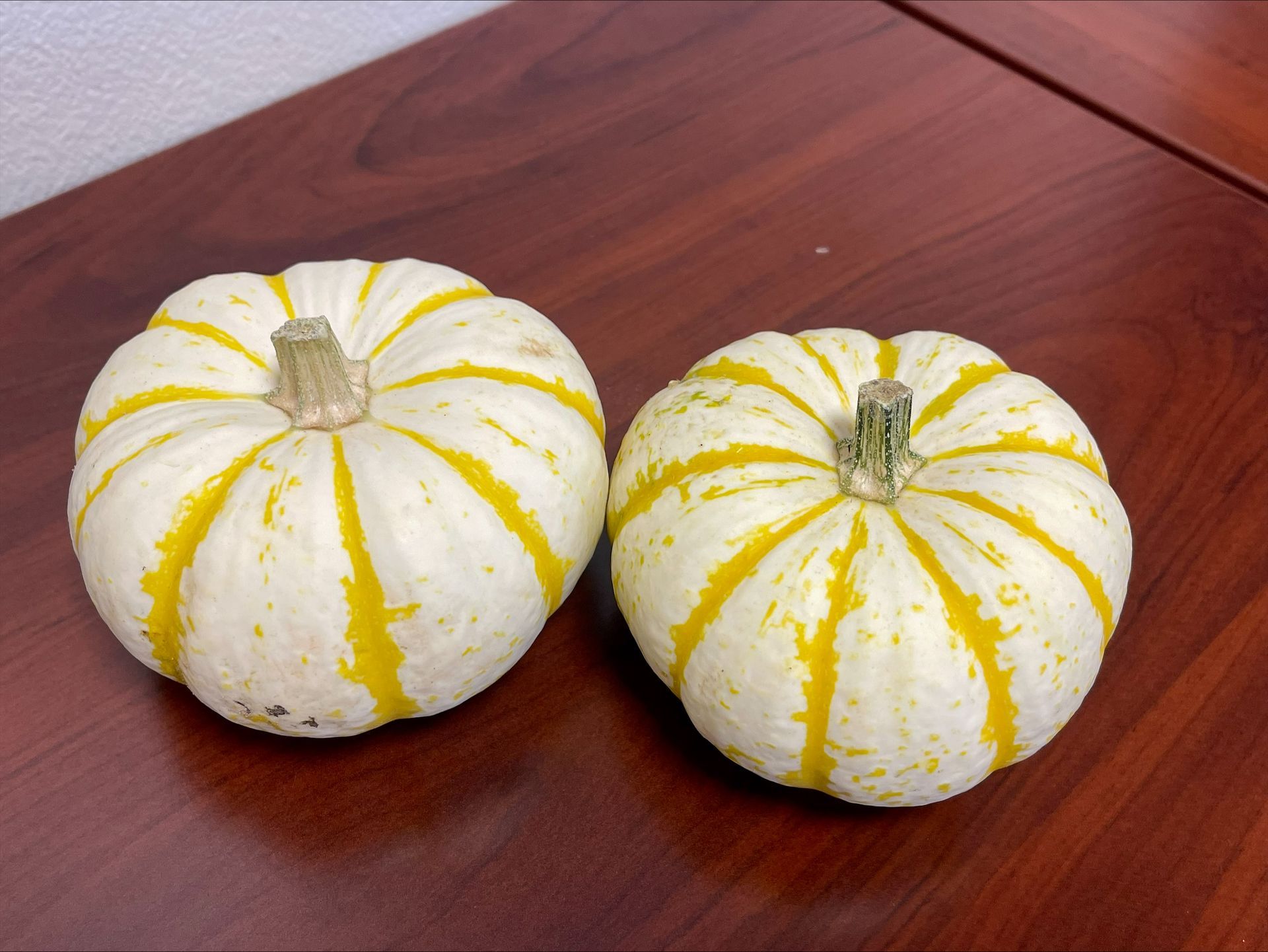 Two small, white pumpkins with yellow stripes on a brown wooden table.