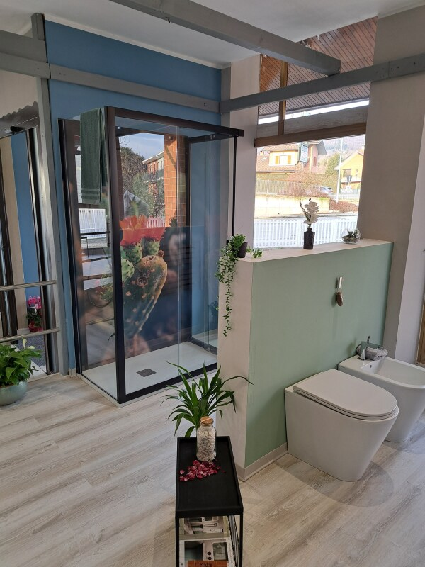 Espositore per box doccia con cornice nera, WC, bidet e piante. Pavimento effetto legno chiaro e pareti verde chiaro.