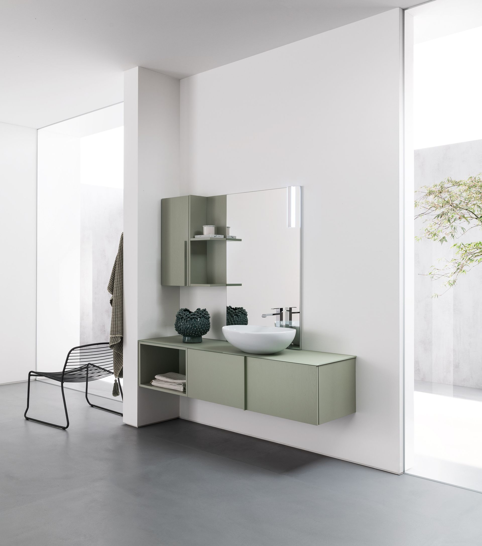 Bagno moderno con mobile lavabo sospeso verde chiaro, specchio e mensole su pareti bianche; pavimento grigio.