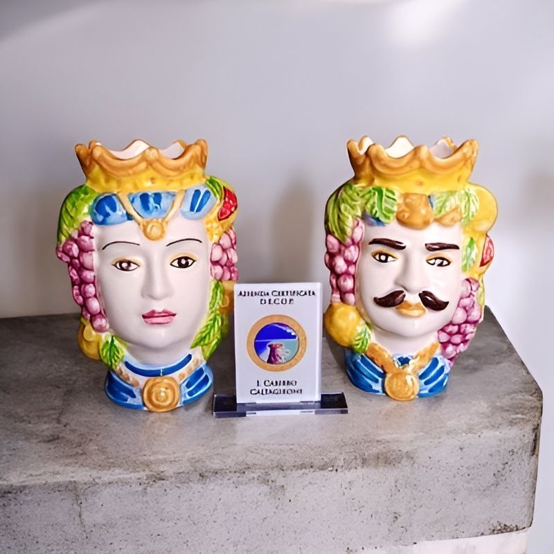 Due vasi in ceramica siciliana a forma di testa, uno maschile e uno femminile, con corone, uva e dettagli blu. Tra di essi è presente un certificato di autenticità.