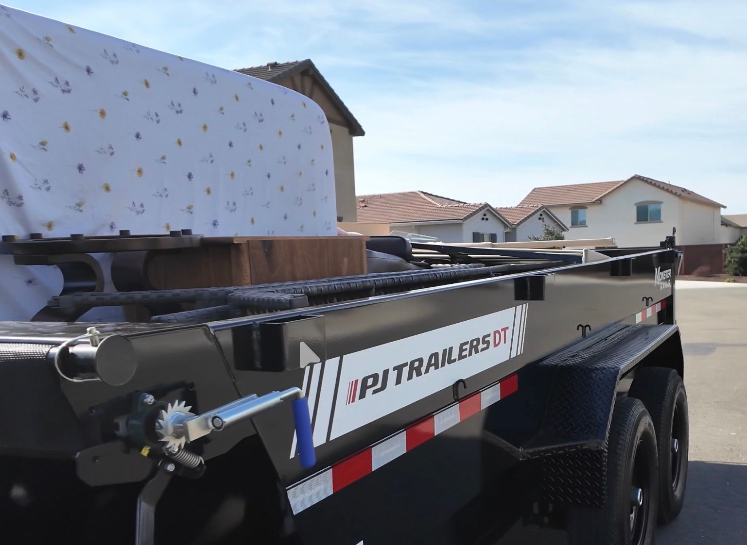 Flatbed trailer loaded with large gray metal equipment in a residential driveway under a cloudy sky