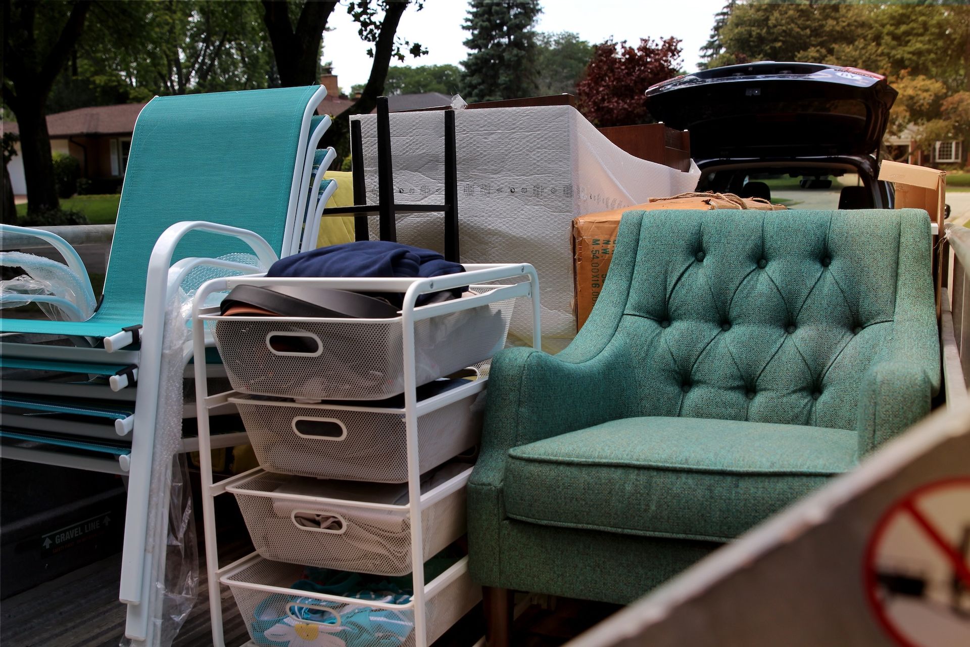 Outdoor yard sale display with teal chairs, wicker drawers, and a mint green tufted loveseat