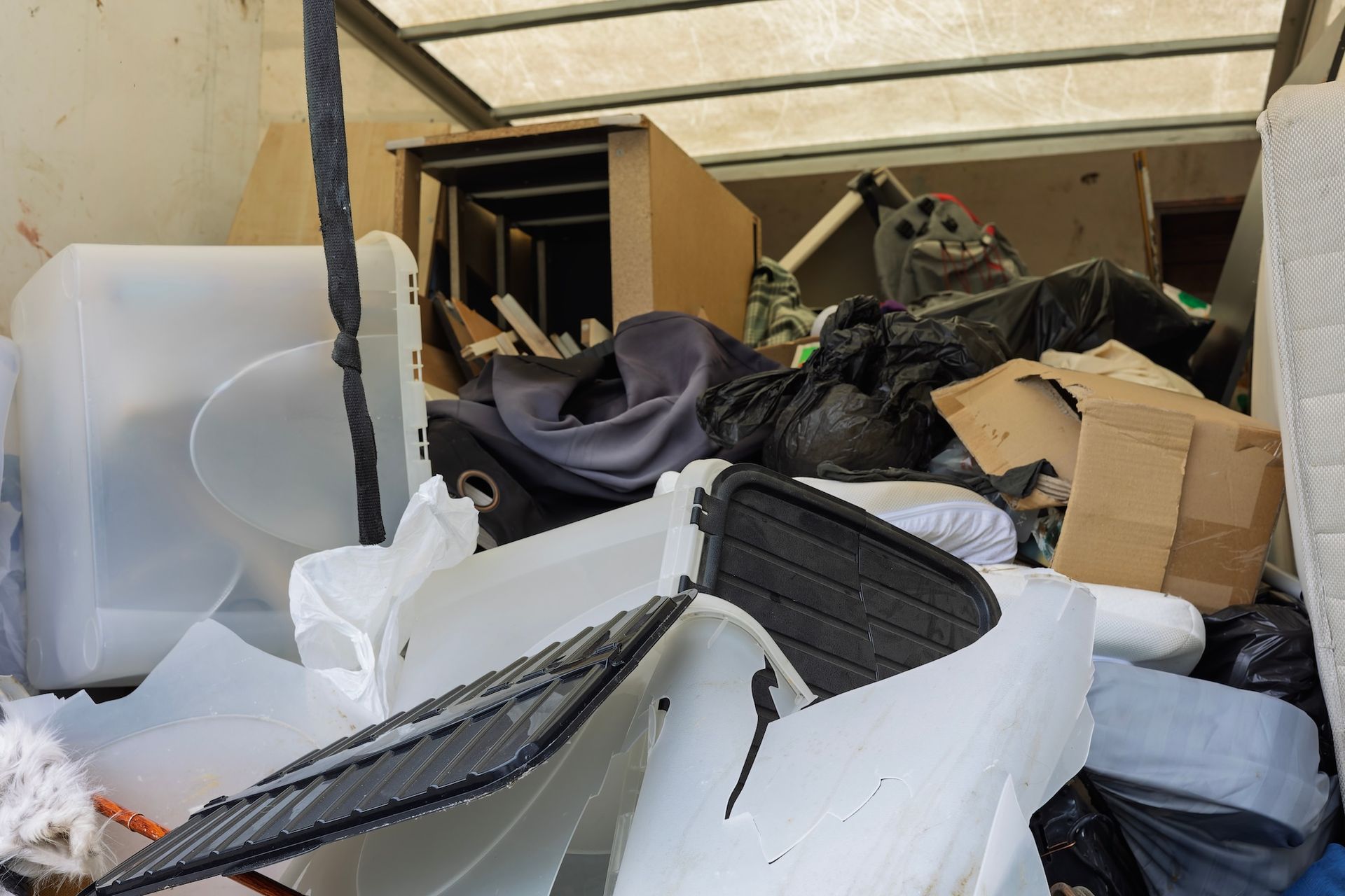Overflowing dumpster filled with broken furniture, cardboard, and debris under a covered area