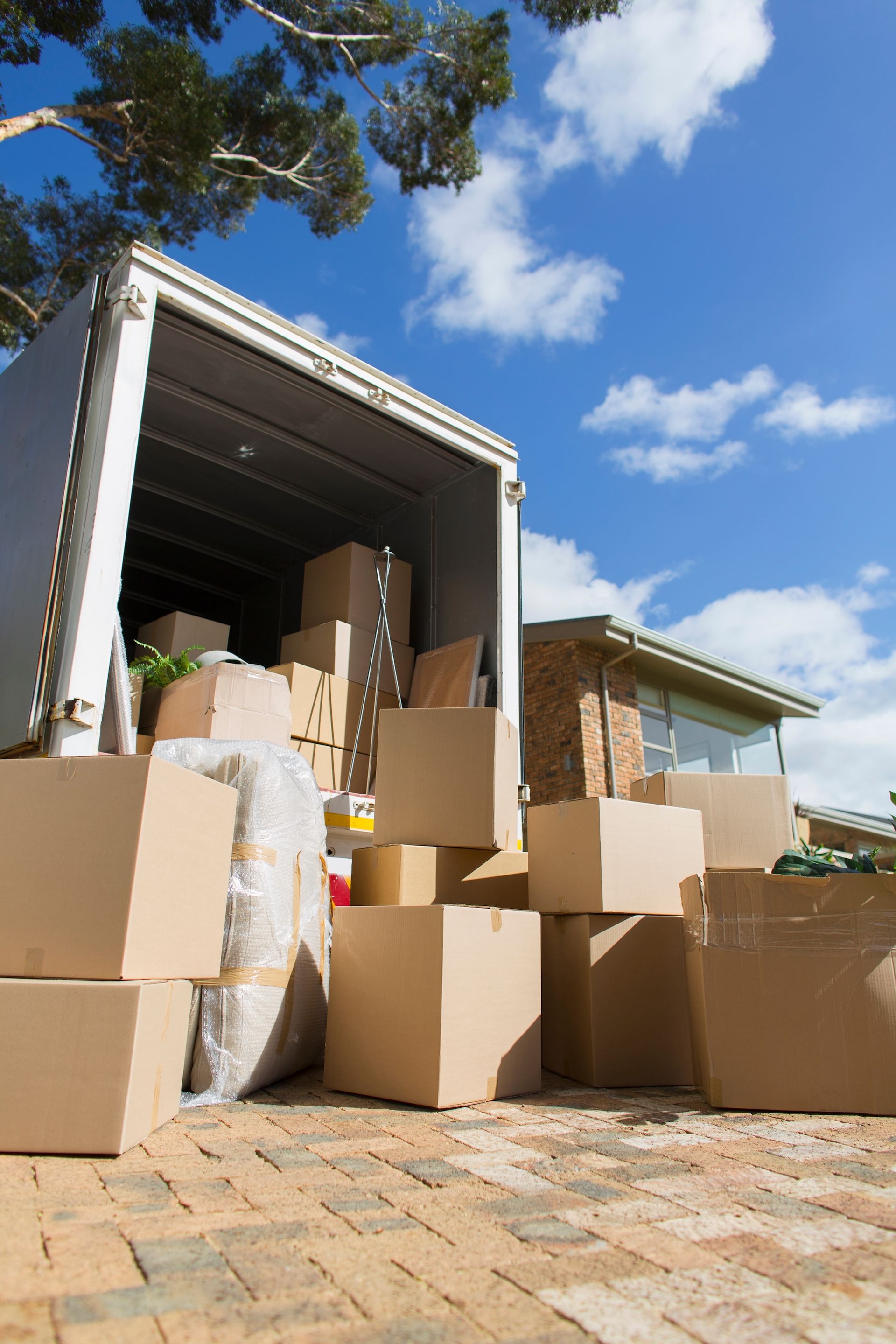 Moving truck unloading stacked cardboard boxes on a brick driveway under a blue sky