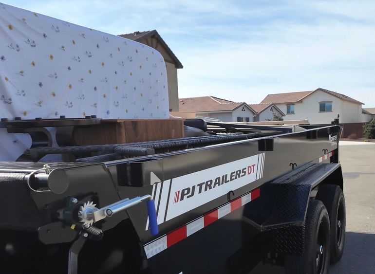 Red utility trailer loaded with black metal frame parts in a residential driveway.