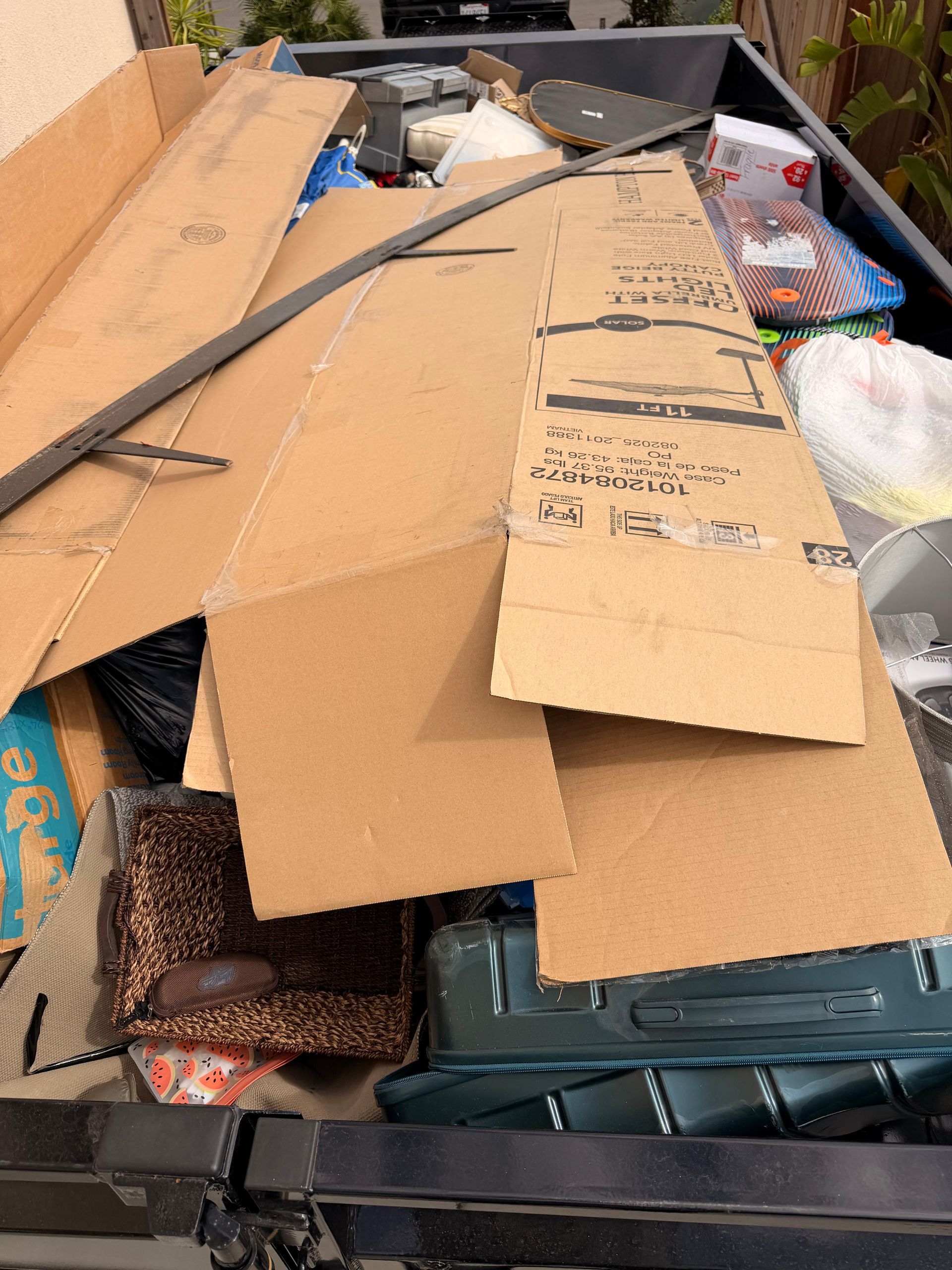 Overflowing trash bin filled with flattened cardboard boxes and mixed waste