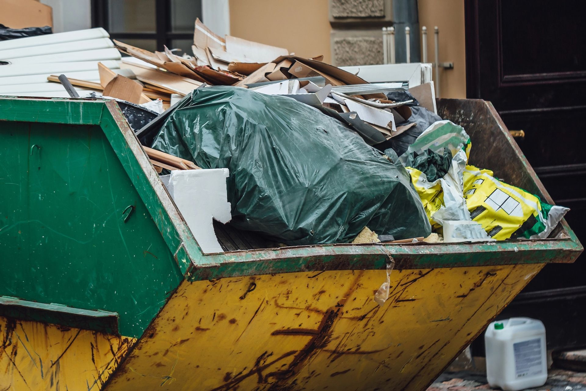 Overflowing construction dumpster with green tarp, cardboard, and debris on a street